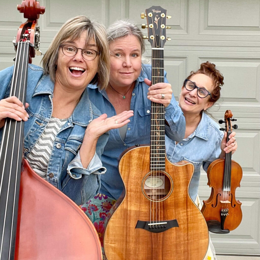 3 smiling women holding upright bass, guitar and fiddle